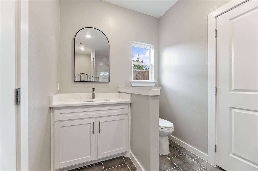 1242 Seminole Drive, Dallas, TX 75217 Bathroom featuring white shaker-style cabinetry, white stone-composite countertop with integrated sink, arched wall mirror, and porcelain tile flooring