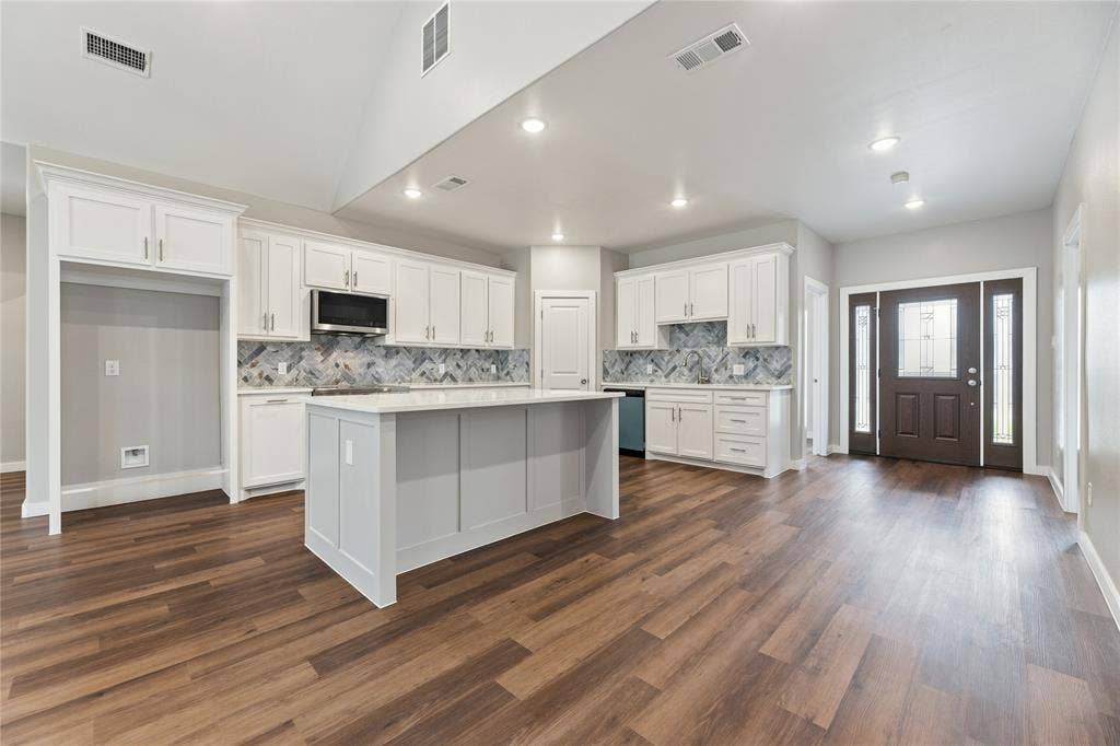 1242 Seminole Drive, Dallas, TX 75217 Kitchen featuring a vaulted ceiling, white cabinetry, a center island with solid surface countertops, herringbone pattern tile backsplash, and wood-finish flooring