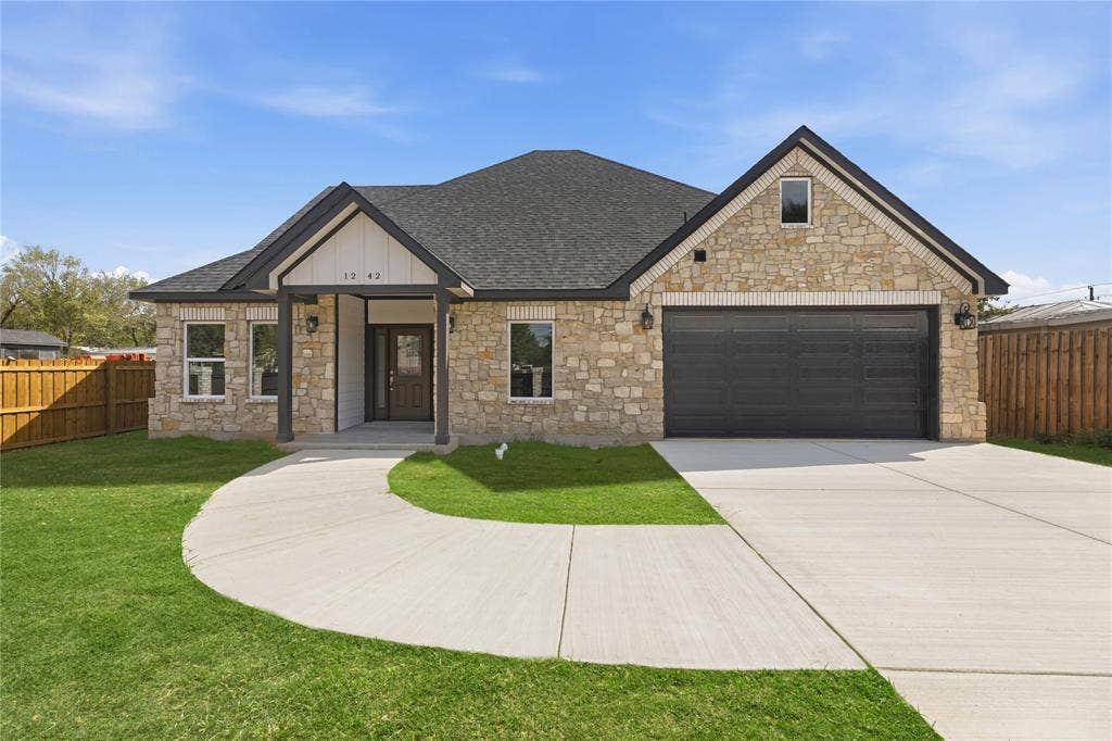 1242 Seminole Drive, Dallas, TX 75217 Stone veneer exterior with dark-finish gabled roof, concrete driveway, two-car garage, and wood-toned privacy fencing