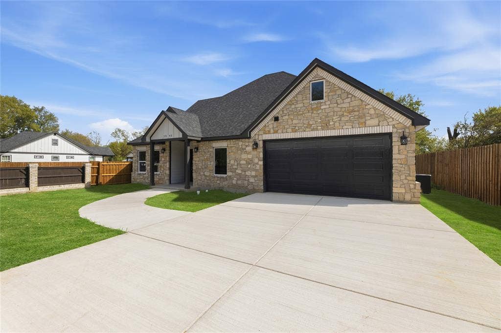 1242 Seminole Drive, Dallas, TX 75217 Stone masonry exterior with a multi-gabled asphalt shingle roof, two-car garage with dark-finish door, and concrete driveway