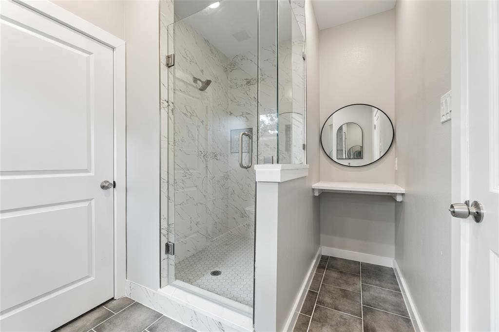 1242 Seminole Drive, Dallas, TX 75217 Walk-in shower with floor-to-ceiling stone-look tile, glass enclosure, hexagonal mosaic tile flooring, built-in shelving, and circular wall-mounted mirror