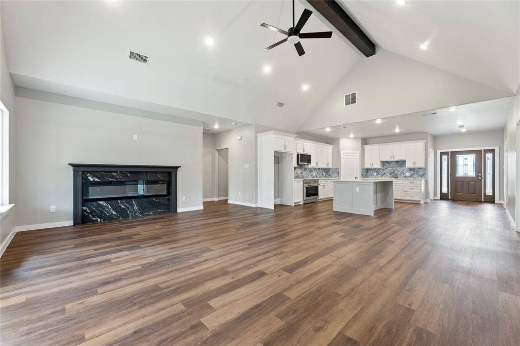 1242 Seminole Drive, Dallas, TX 75217 Vaulted ceilings with exposed structural beam, wood-finish flooring, stone-surround fireplace, kitchen with white cabinetry and central island, and recessed lighting