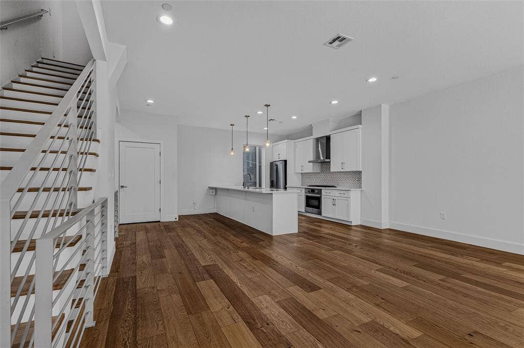 2222 Moser Avenue, #105, Dallas, TX 75206 Open-concept interior featuring wood-finish flooring, recessed lighting, and a kitchen equipped with white cabinetry, a center island, and stainless steel appliances, accented by a staircase with horizontal metal railing