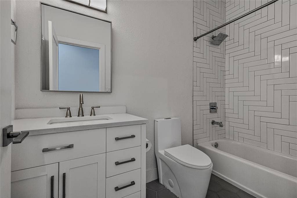 2222 Moser Avenue, #105, Dallas, TX 75206 Bathroom featuring a white vanity with a composite countertop, rectangular undermount sink, herringbone tile shower surround, and dark hexagonal floor tile