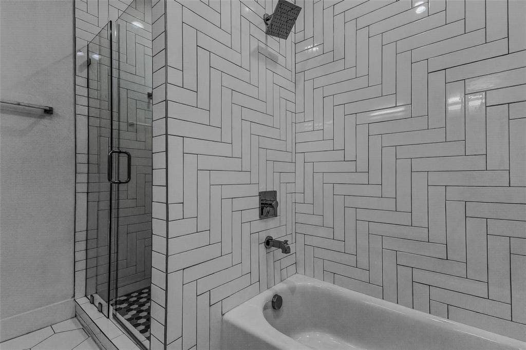 2222 Moser Avenue, #105, Dallas, TX 75206 Shower and bathtub combination featuring white rectangular wall tile in a herringbone pattern, a glass shower enclosure, a rainfall showerhead, and metallic fixtures