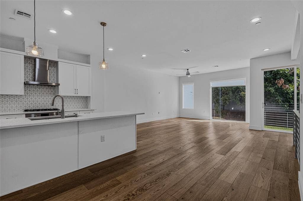 2222 Moser Avenue, #105, Dallas, TX 75206 Open-concept kitchen featuring a stone-topped island, geometric patterned tile backsplash, stainless steel range hood, recessed ceiling lighting, and wide-plank wood-finish flooring