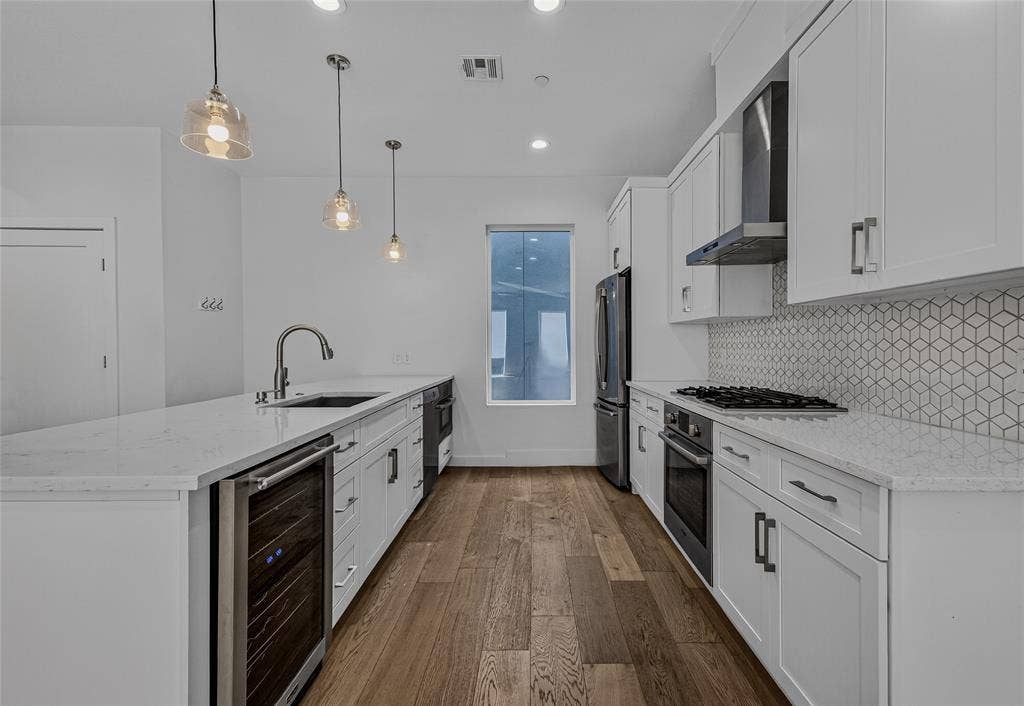 2222 Moser Avenue, #105, Dallas, TX 75206 Kitchen featuring white cabinetry, quartz countertops, geometric tile backsplash, stainless steel appliances including a built-in wine cooler, and wood-finish flooring