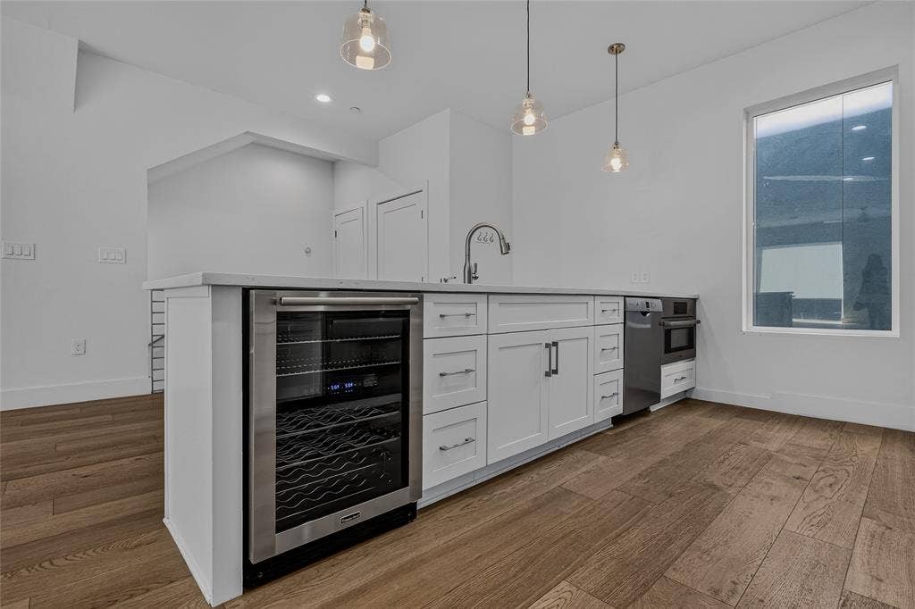 2222 Moser Avenue, #105, Dallas, TX 75206 Kitchen island featuring white shaker-style cabinetry, an integrated stainless steel wine refrigerator, a high-arc faucet, quartz countertops, and wood-finish flooring