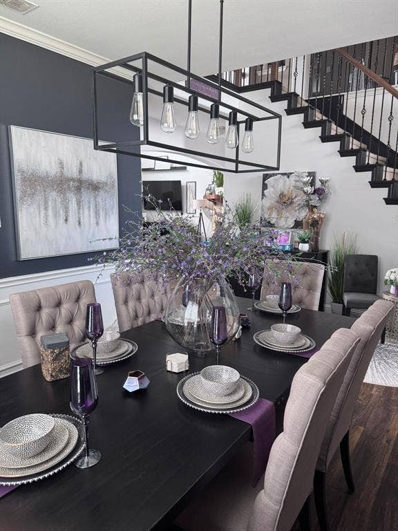 Dining area featuring a linear matte black chandelier, dark accent wall with chair rail molding, and an open staircase with black metal balusters and wood-finish treads