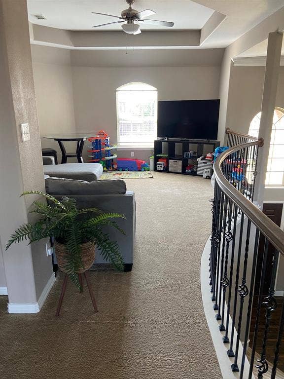 Tray ceiling with integrated fan, carpeted flooring, and wrought iron spindle railing