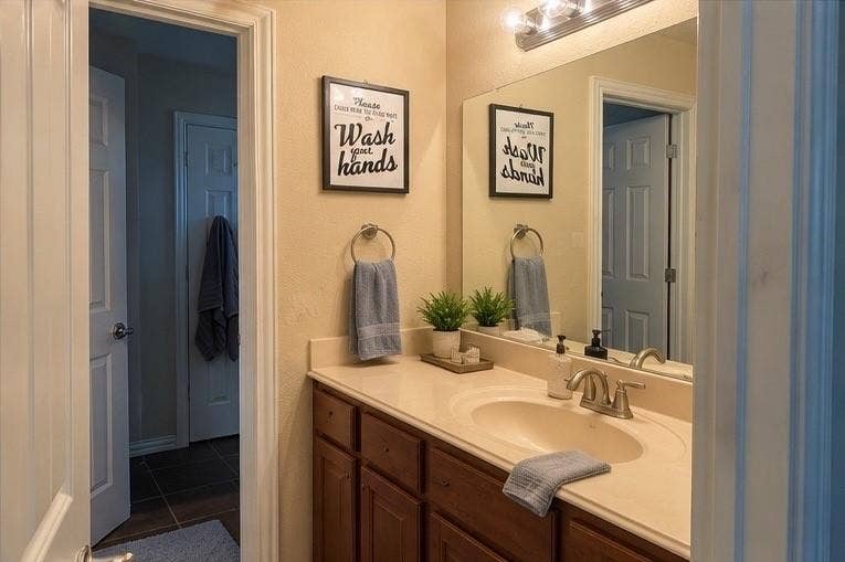 Bathroom vanity featuring dark-tone wood cabinetry, an integrated basin, a polished countertop, a large wall-mounted mirror, and multi-bulb vanity lighting