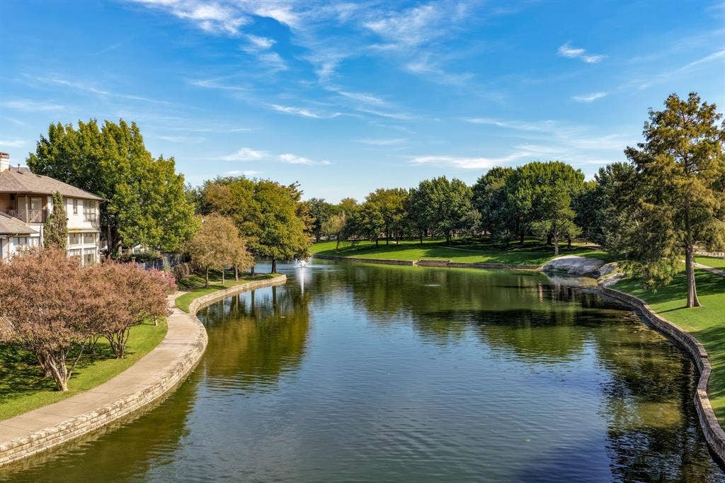 Waterfront property featuring a stone-lined canal, manicured green space, mature trees, and a central water fountain