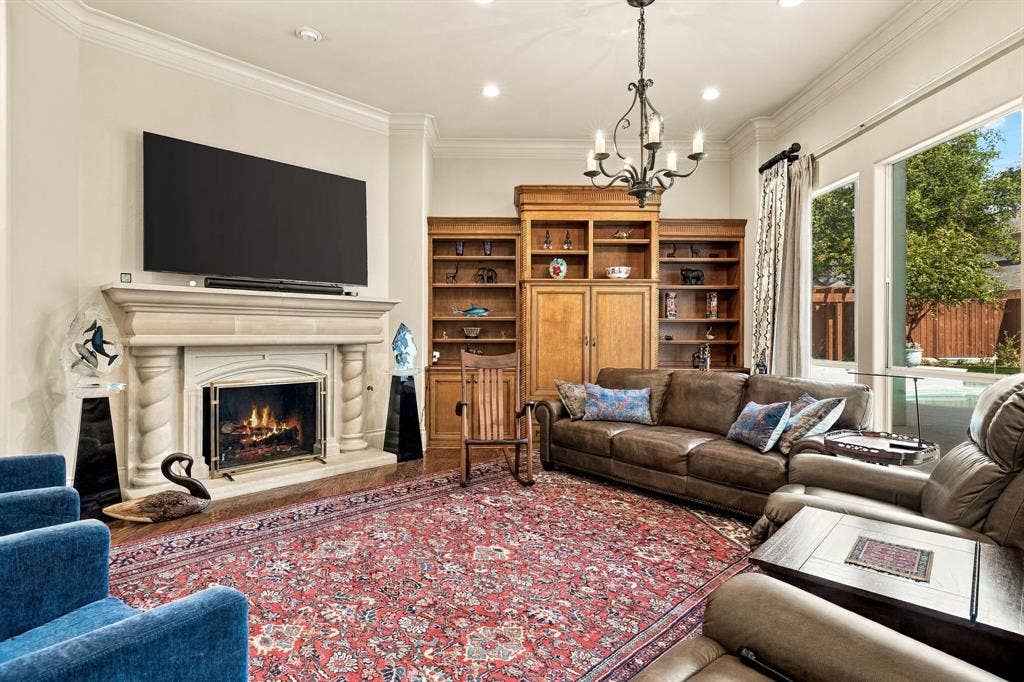 Stone fireplace with decorative columns, custom built-in wood cabinetry, recessed lighting, wrought iron chandelier, and oversized windows