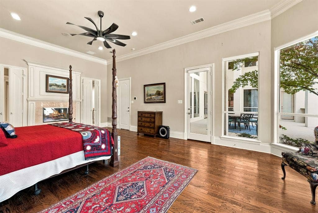 Spacious interior featuring wood-finish flooring, a fireplace with a custom mantel, crown molding, a modern multi-blade ceiling fan, and large windows