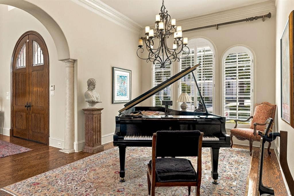 Classic crown molding, wrought iron multi-arm chandelier, and arched windows with plantation shutters