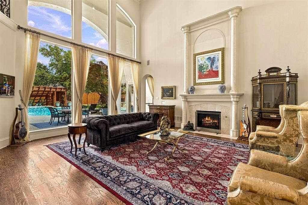 Vaulted ceilings, expansive floor-to-ceiling windows, wood-finish flooring, and a fireplace with a decorative stone mantle