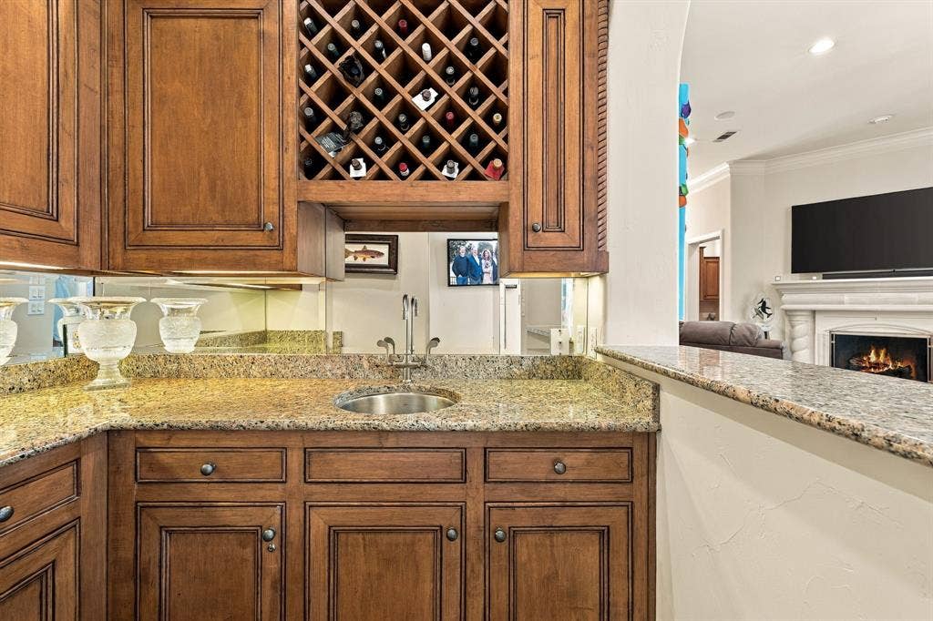 Custom wet bar featuring stained wood cabinetry, integrated lattice wine storage, a stone countertop, a circular stainless steel undermount sink, and a mirrored backsplash