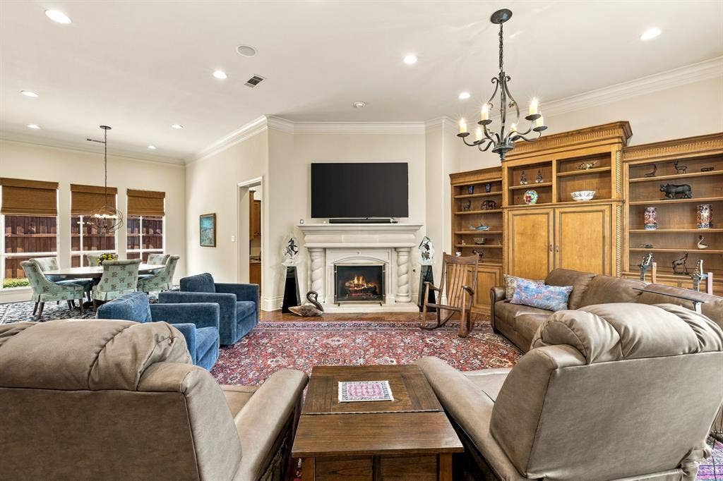 Living area featuring a stone fireplace with decorative columns, extensive floor-to-ceiling built-in wood shelving, recessed lighting, and a wrought-iron chandelier