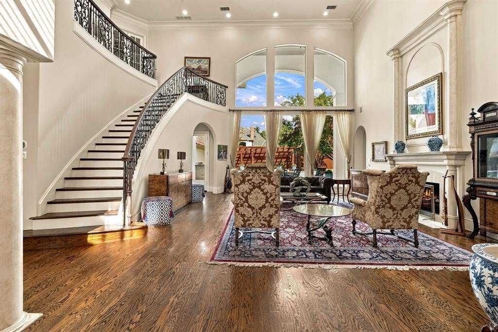 Grand foyer featuring high ceilings, arched windows, wood-finish flooring, a curved staircase with ornate iron railings, and a fireplace with a decorative mantel