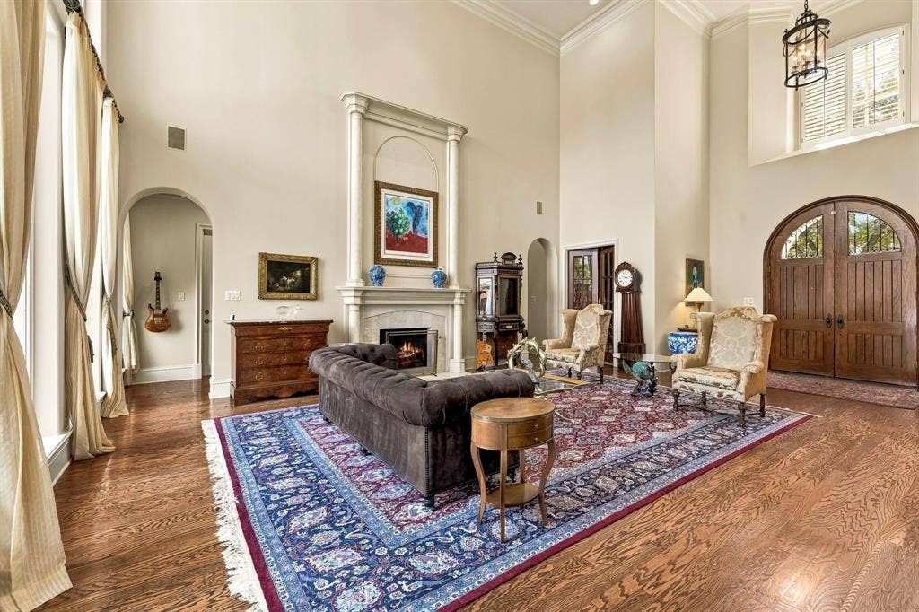 Expansive room with vaulted ceilings featuring a floor-to-ceiling fireplace mantel, arched entryways, wood-finish flooring, and arched double wooden entry doors