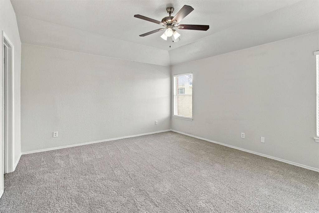 Room with high tray ceiling, neutral wall-to-wall carpeting, and a multi-blade ceiling fan with integrated lighting fixture