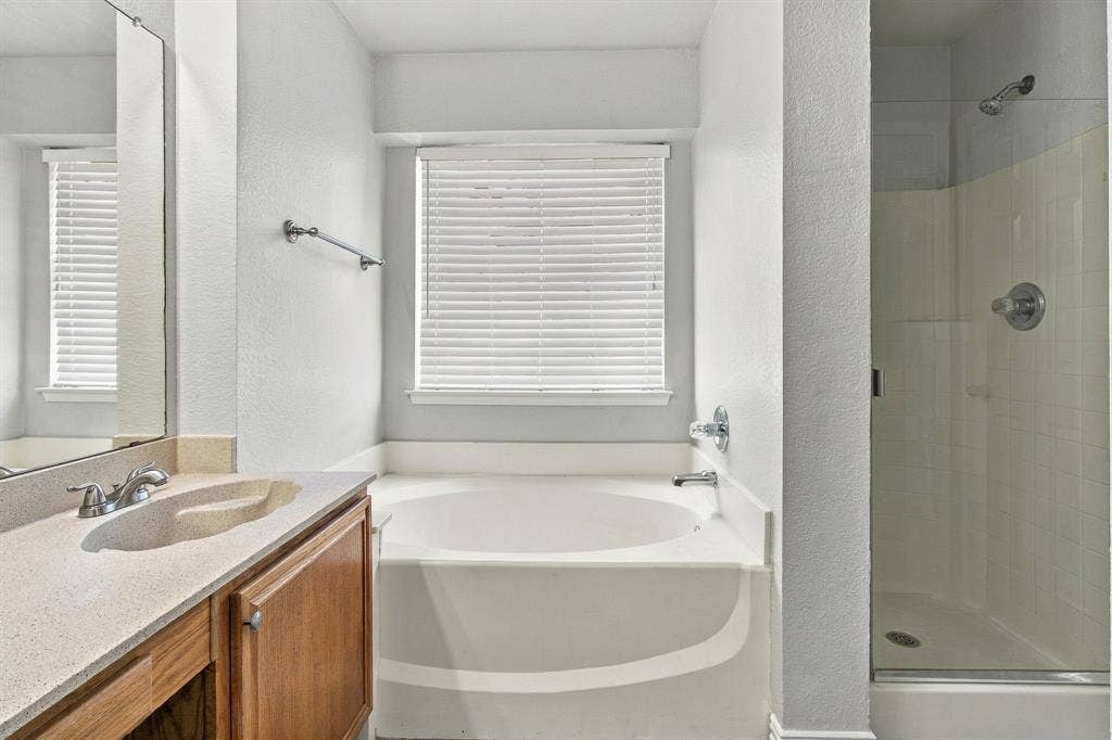 Bathroom featuring a wood-finish vanity with an integrated sink and countertop, a soaking tub, and a glass-enclosed shower with a chrome fixture