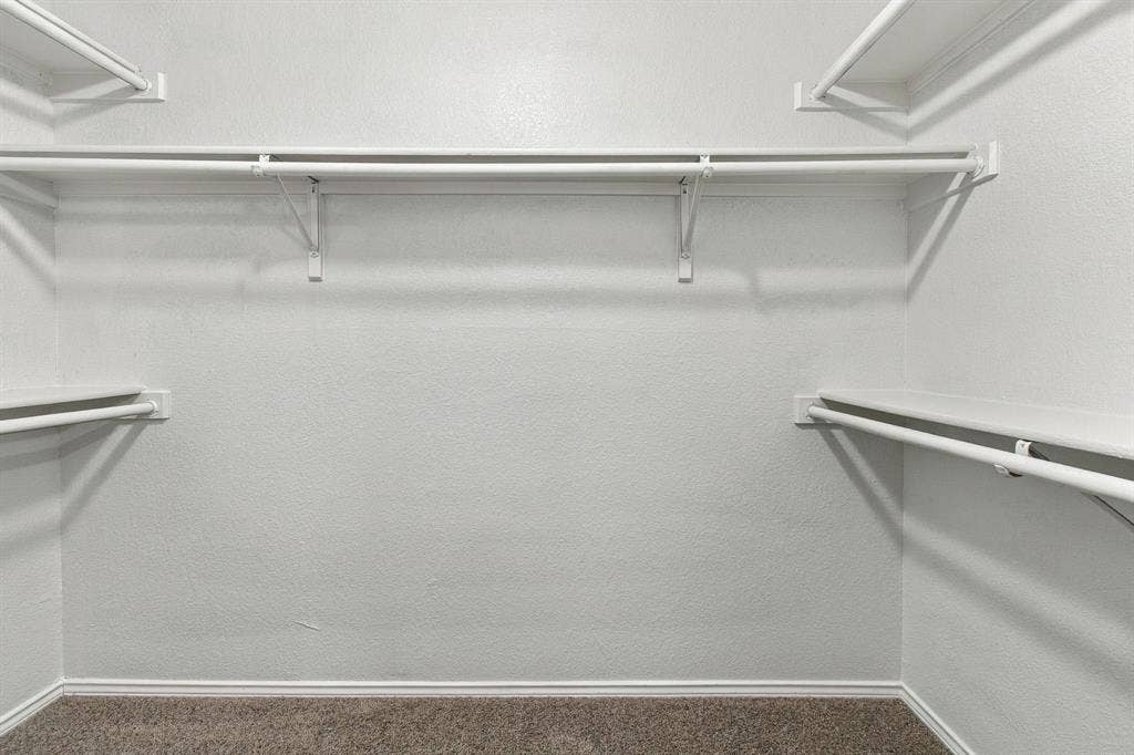 Storage area featuring white wire shelving units, dual-level hanging rods, and neutral carpeting