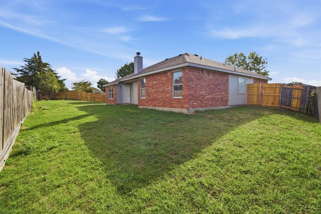 Rear exterior featuring red brick and siding facade, chimney, fenced perimeter, and grass lawn