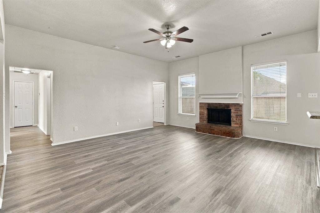 Living area featuring high ceilings, wood-finish flooring, a brick fireplace with a mantle, and a ceiling fan