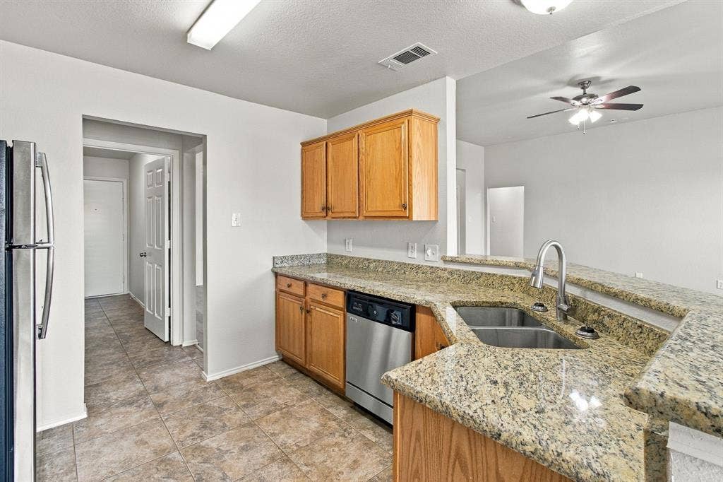 Kitchen featuring stone-finish countertops, stainless steel dishwasher, wood-finish cabinetry, dual-basin stainless steel sink with high-arc faucet, and ceramic tile flooring
