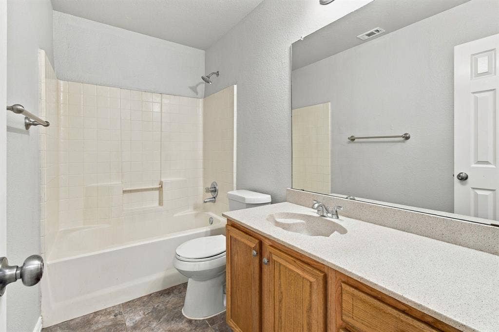 Bathroom featuring a vanity with a light-toned solid surface countertop and integrated sink, wood-finish cabinetry, a large wall-mounted mirror, and a tub-shower combination with tile surround