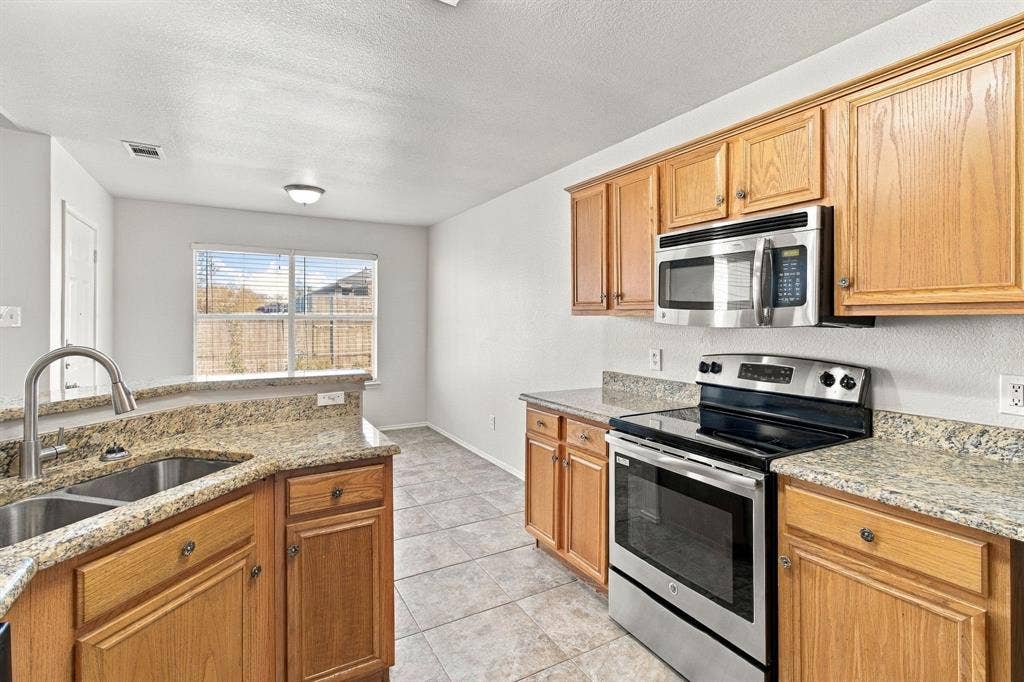 Kitchen featuring medium-tone wood cabinetry, stone-finish countertops, stainless steel microwave, stainless steel range, and stainless steel undermount sink with a gooseneck faucet