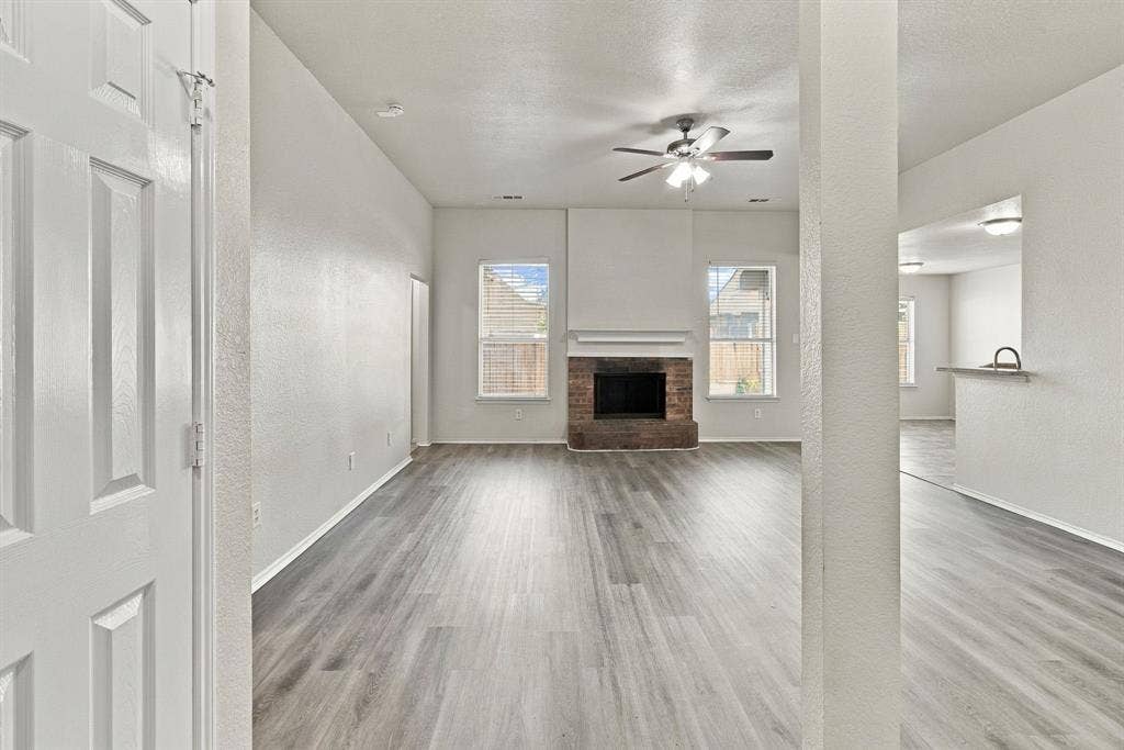 Open-concept room featuring wood-finish flooring, a brick fireplace with a mantel, dual windows, and a ceiling fan with integrated lighting