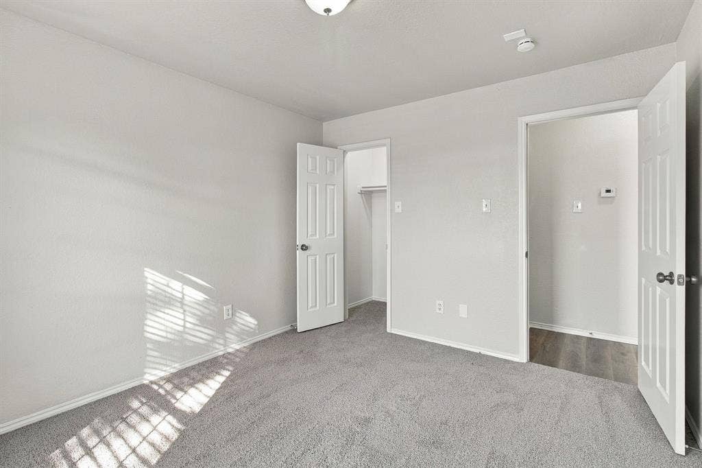 Interior room featuring neutral-toned carpeting, six-panel interior doors, a walk-in closet, and a ceiling-mounted light fixture