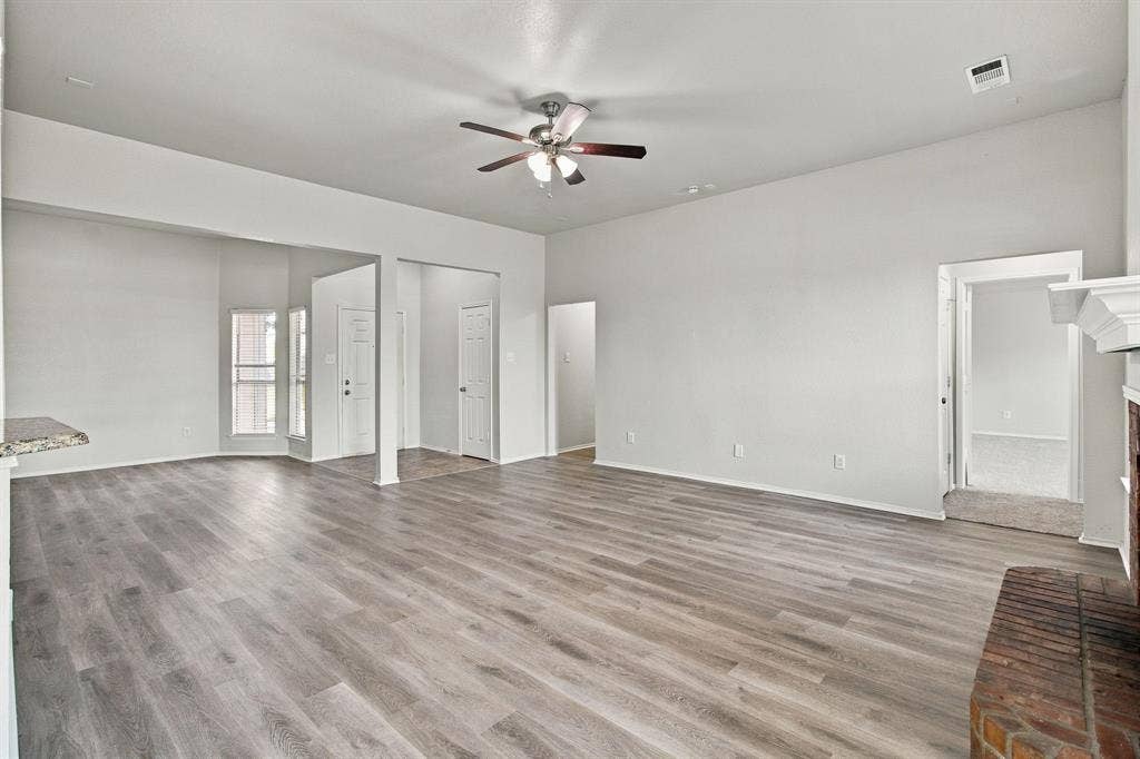 Open interior space featuring wood-finish flooring, vaulted ceilings, a central ceiling fan with integrated lighting, and a brick fireplace hearth