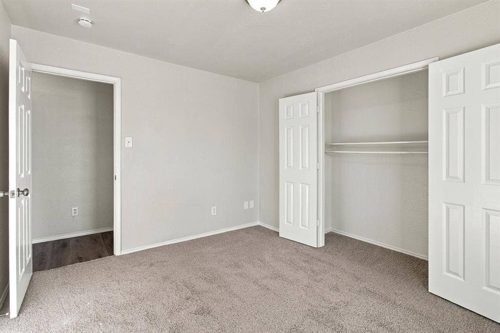 Neutral-toned room featuring neutral carpeting, six-panel interior doors, a closet with built-in shelving, and a dome ceiling light fixture