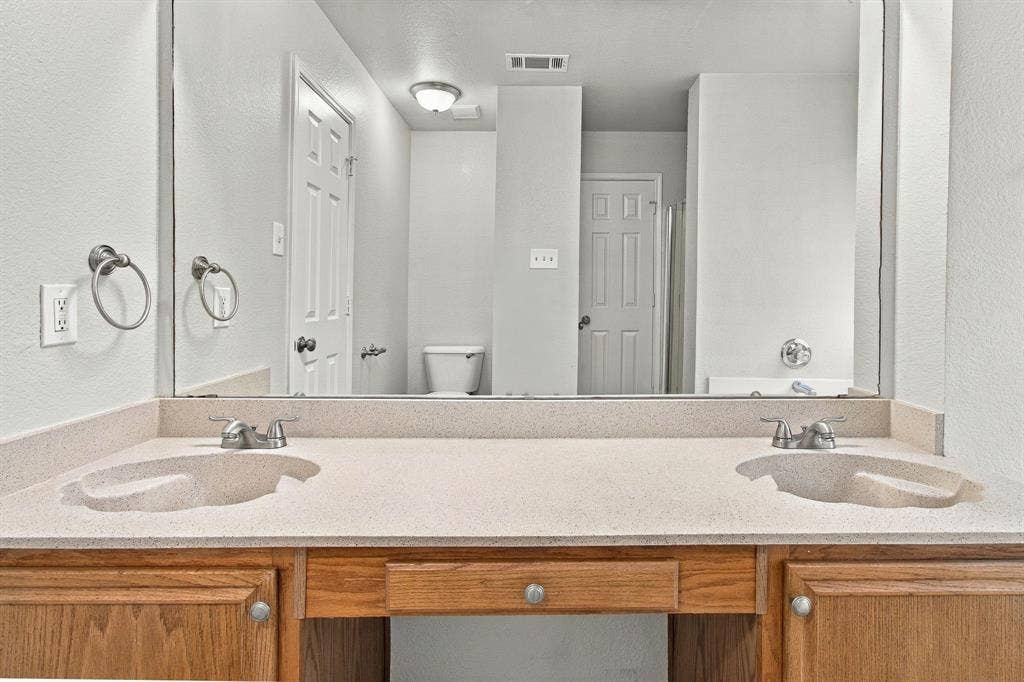 Dual-sink vanity with integrated countertop, wood-finish cabinetry, and large wall-mounted mirror