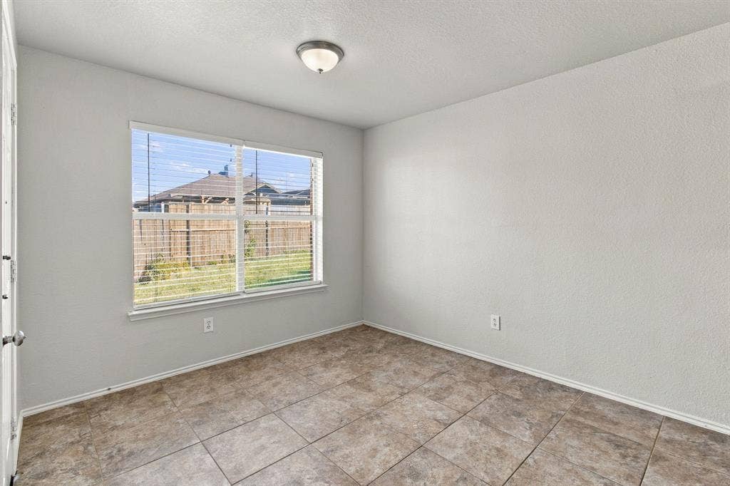 Neutral interior room featuring tile flooring, smooth-textured walls, a large window, and a flush-mount ceiling light fixture
