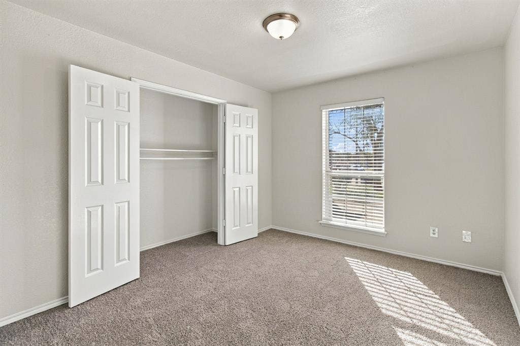 Neutral wall tones, wall-to-wall carpeting, window with slatted blinds, and double-door closet with built-in shelving