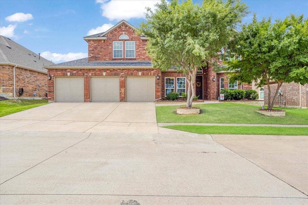 319 Westphalian Drive, Celina, TX 75009 Two-story brick exterior featuring a three-car garage, concrete driveway, and established front landscaping with mature trees and stone-ringed planting beds