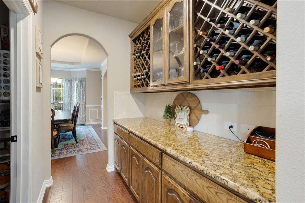 319 Westphalian Drive, Celina, TX 75009 Built-in wine storage cabinetry with glass-front display, substantial countertop space, wood-finish flooring, and an arched doorway framing a dining area
