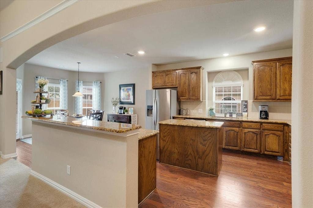 319 Westphalian Drive, Celina, TX 75009 Open-concept kitchen with wood-finish flooring, granite countertops, wood cabinetry, a central island, and stainless steel appliances