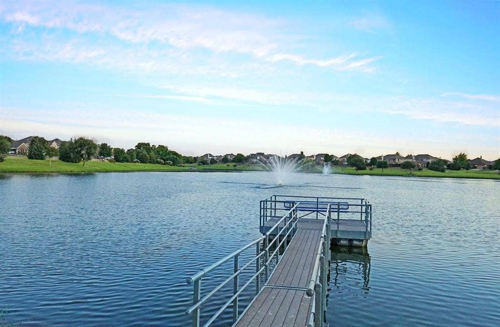 319 Westphalian Drive, Celina, TX 75009 Floating dock with metal railings extending into a body of water featuring two active fountains, surrounded by a manicured green shoreline and residential properties
