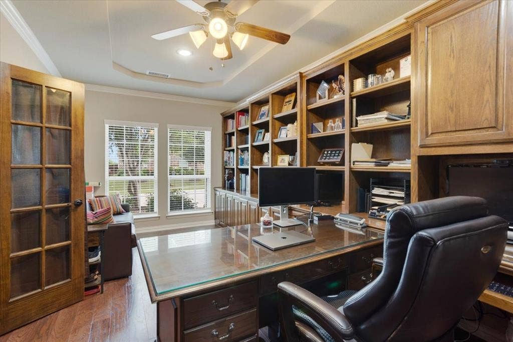 319 Westphalian Drive, Celina, TX 75009 Dedicated office space featuring extensive built-in wood cabinetry and shelving, a tray ceiling with a ceiling fan, wood-finish flooring, and a glass-paneled entry door