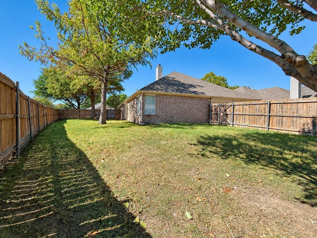 7514 Naples Lane, Frisco, TX 75035 Fenced backyard featuring a brick exterior, shingle roof, chimney, and mature trees