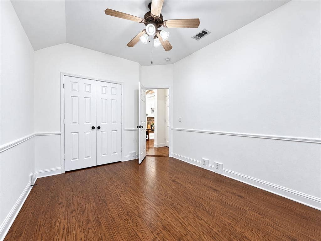 7514 Naples Lane, Frisco, TX 75035 Room featuring wood-finish flooring, a vaulted ceiling, double-panel closet doors, chair rail molding, and a ceiling fan with integrated lighting