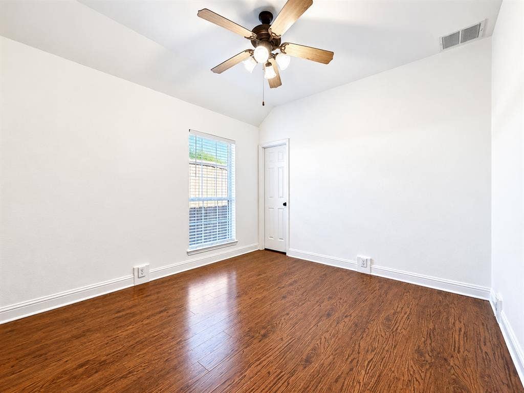 7514 Naples Lane, Frisco, TX 75035 Vaulted ceiling room featuring wood-finish flooring, a central multi-blade ceiling fan with integrated lighting, and a single-panel interior door