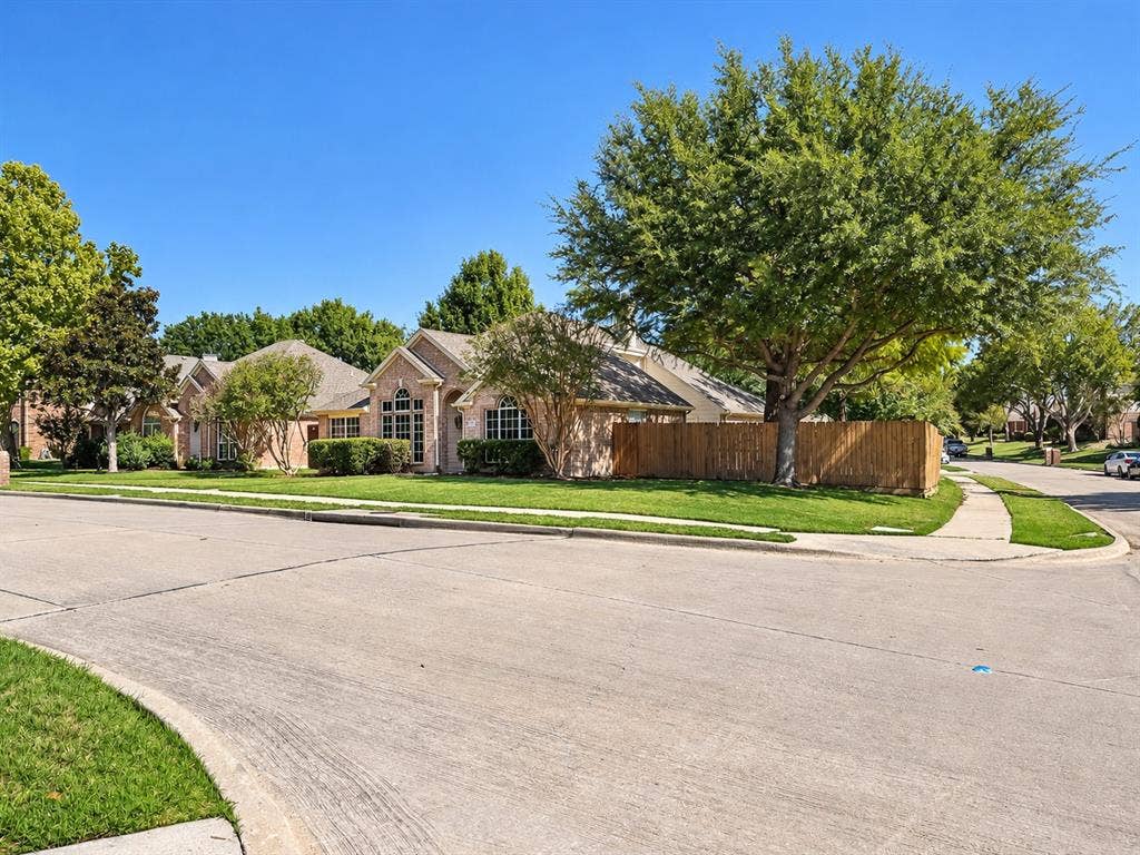 7514 Naples Lane, Frisco, TX 75035 Corner lot residence featuring a brick facade, arched window detailing, wood-finish privacy fencing, and mature trees