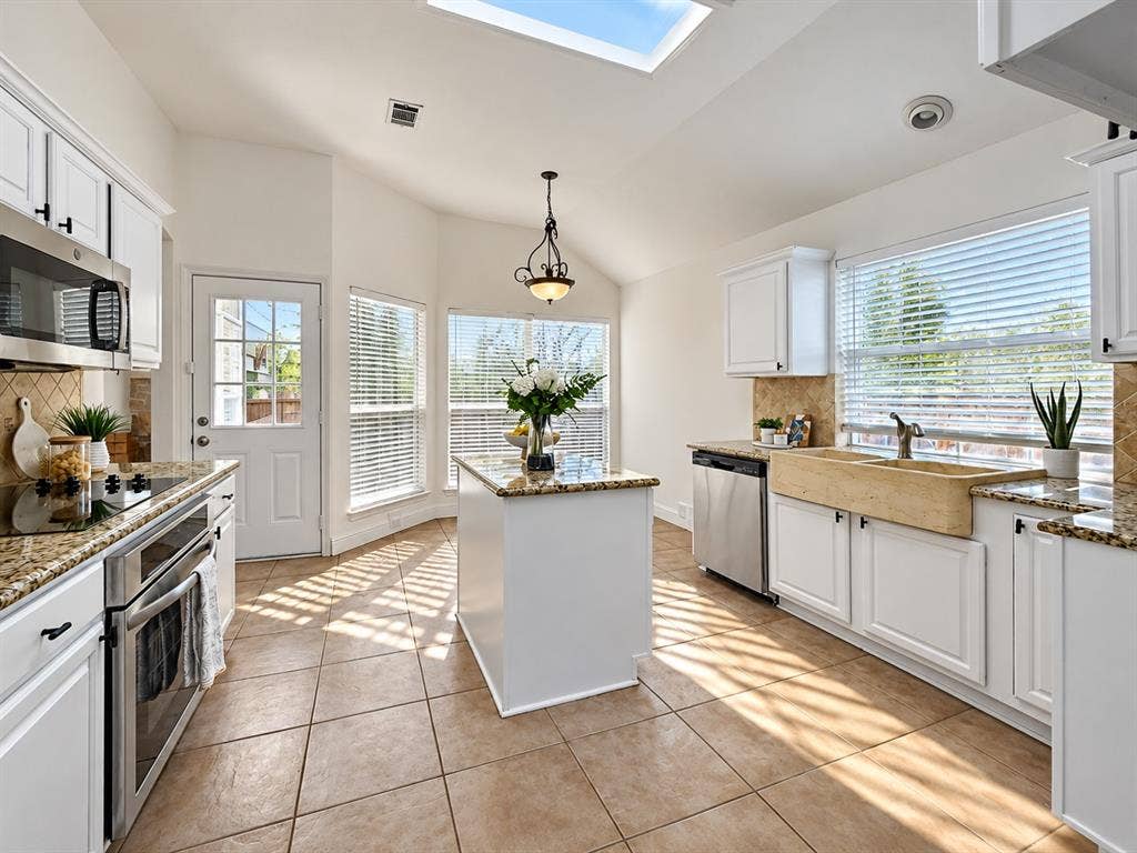7514 Naples Lane, Frisco, TX 75035 Kitchen featuring white cabinetry, stone-surface countertops, central island, farm-style sink, and skylight