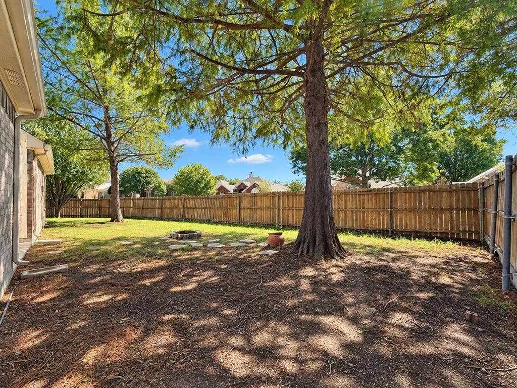 7514 Naples Lane, Frisco, TX 75035 Rear yard featuring mature trees, wood privacy fencing, a stone-bordered fire pit, and stone hardscaping